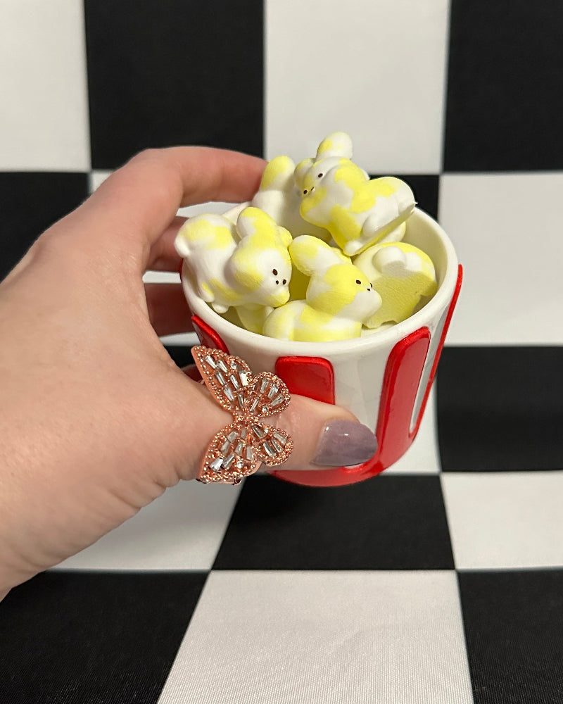 Hand holding a small red cup filled with small white figurines on a black and white checkered background