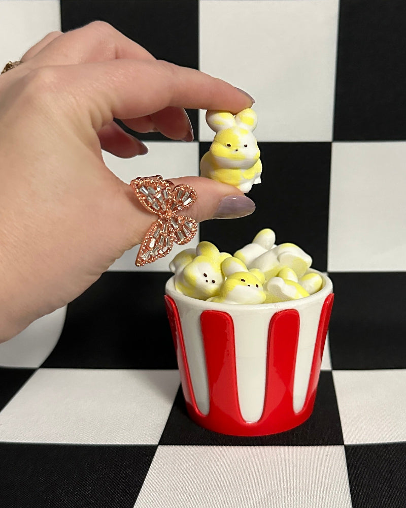 Hand placing a small plush toy into a red and white container on a checkered background