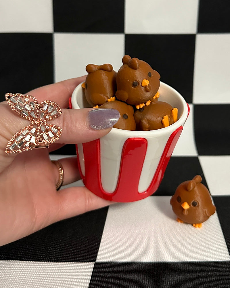 Hand holding a small red and white striped cup filled with chocolate ducks on a black and white checkered background.