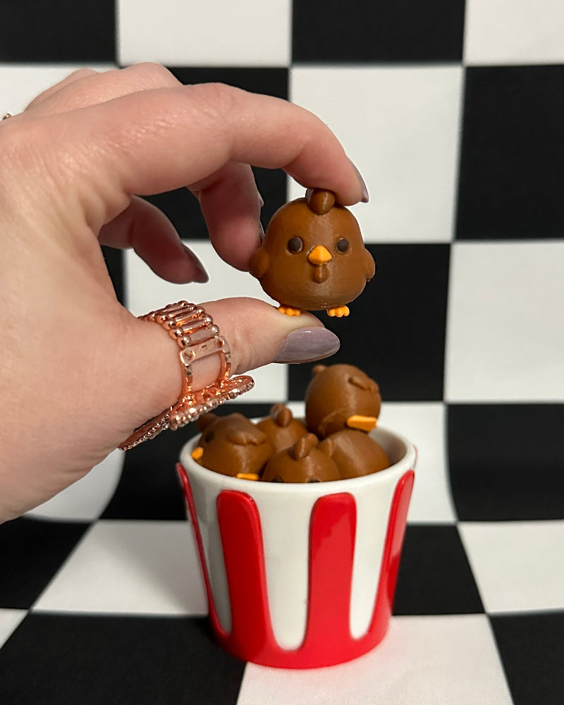 Hand placing a small brown dog toy into a red and white striped cup against a black and white checkered background.
