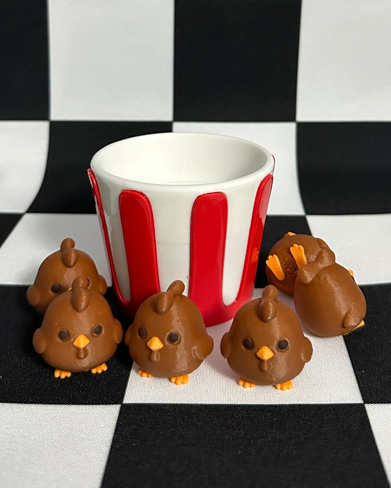 Small brown chick figurines around a red and white striped cup on a black and white checkered background