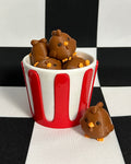 Small brown dog toys in a red and white striped container on a black and white checkered background