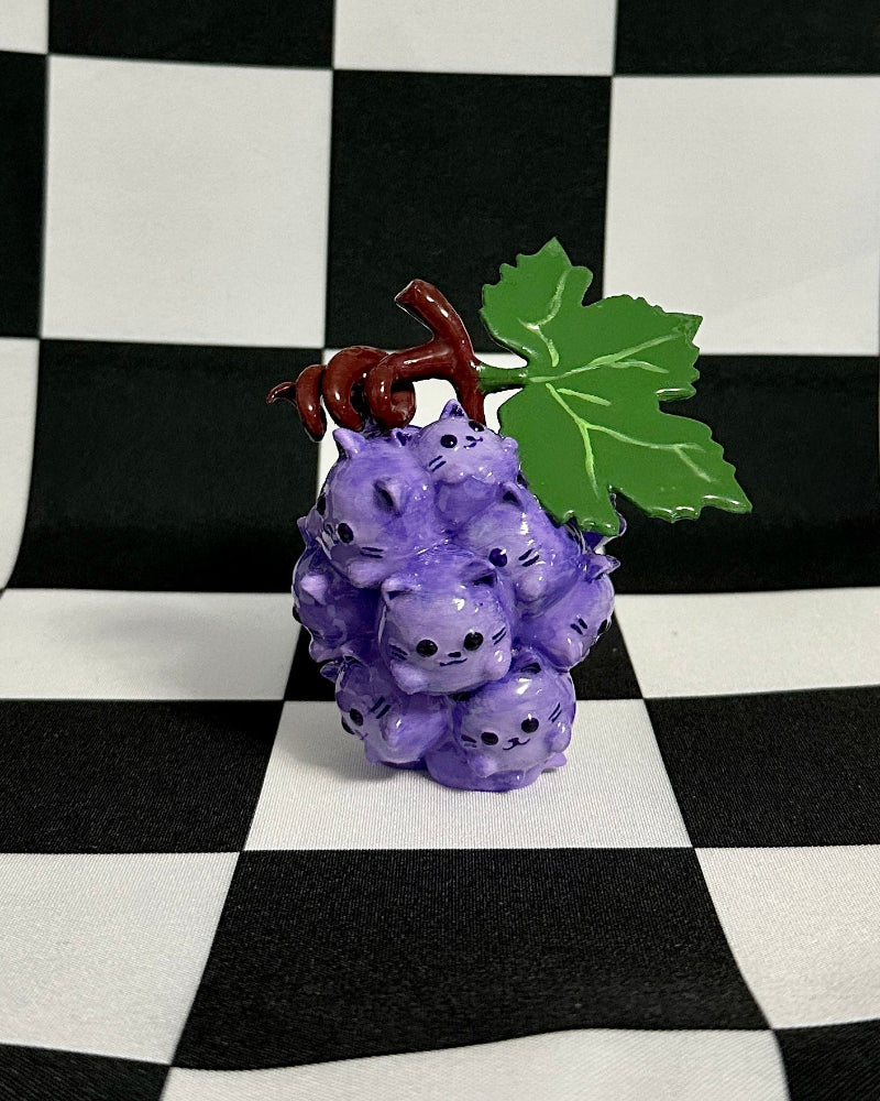 Purple grape-shaped figurine with a green leaf on a checkered black and white background