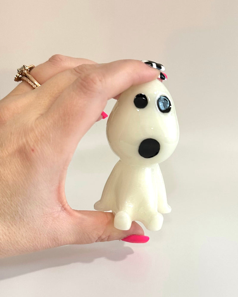 Hand holding a small white figurine with black eyes and mouth against a plain background