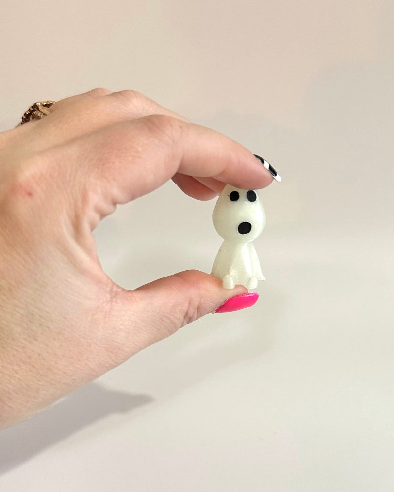 Hand holding a small white figurine with black accents against a plain background