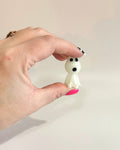 Hand holding a small white figurine with black accents against a plain background
