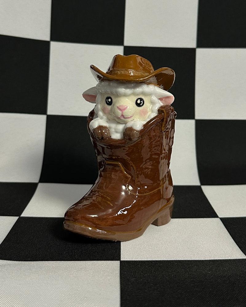 Small figurine of a sheep in a cowboy hat and boots on a checkered background