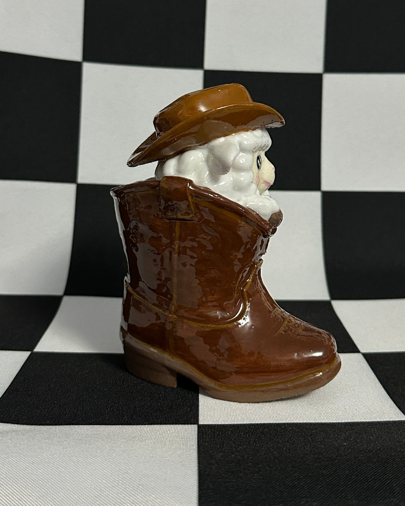 Figurine of a person wearing a brown cowboy hat and boots on a checkered background