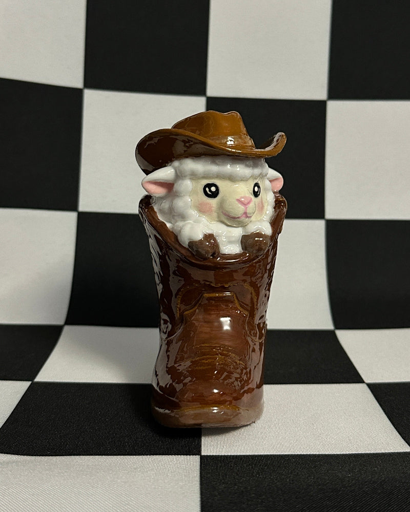 Small white mouse figurine wearing a brown cowboy hat inside a brown boot on a checkered background