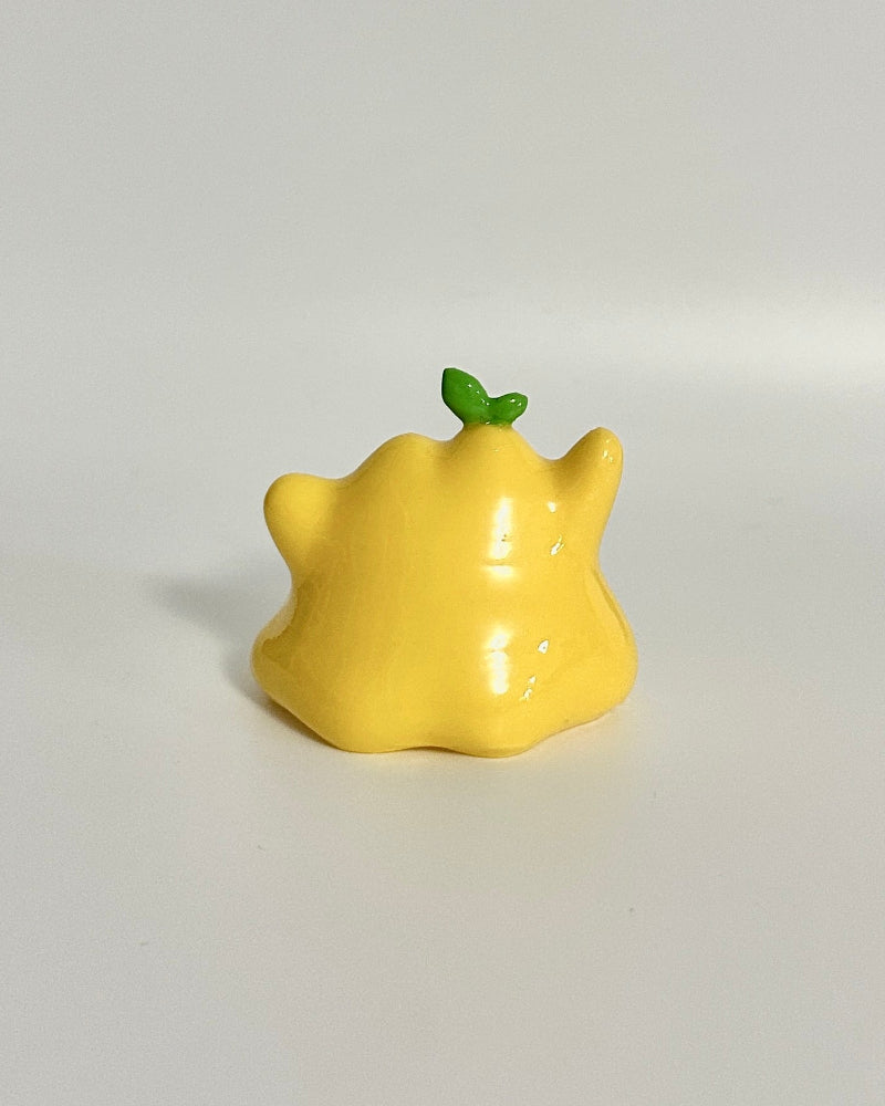 Yellow cat-shaped object with a green leaf on a white surface