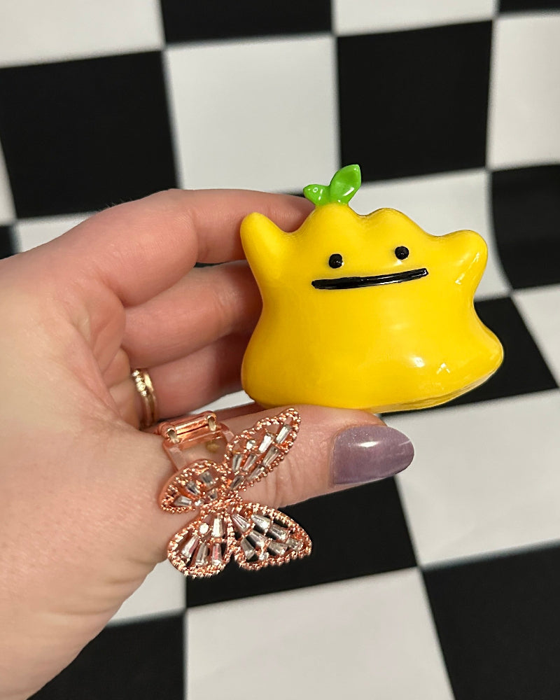 Yellow cartoon-like figurine held by a hand against a black and white checkered background