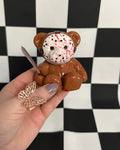 Hand holding a teddy bear with a mask against a checkered background