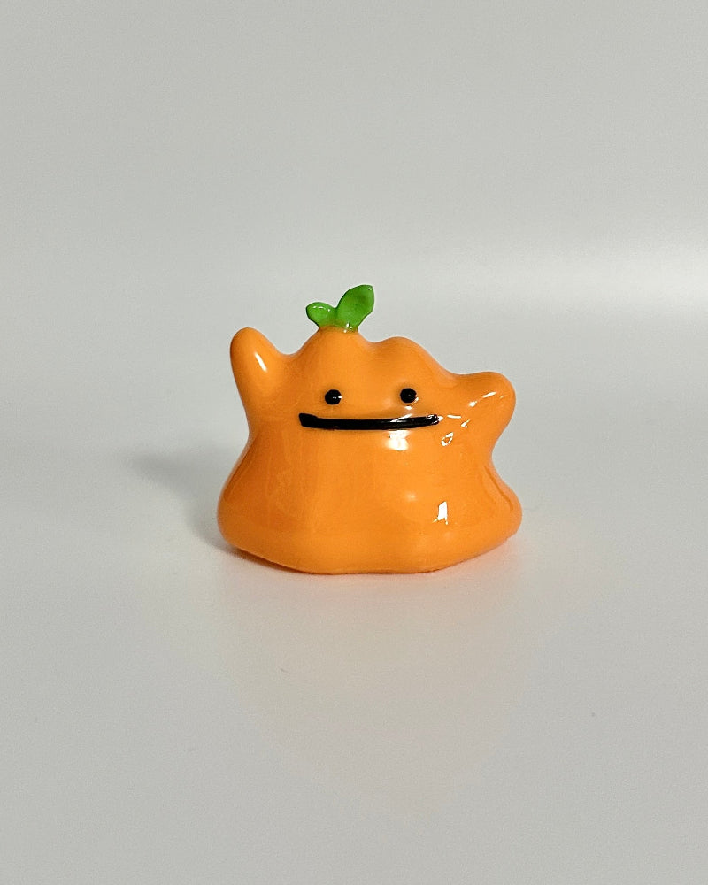Small orange creature figurine with a green leaf on a white background