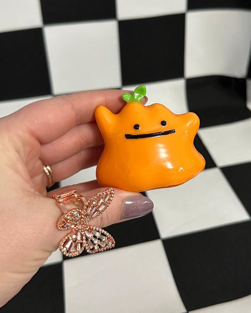 Hand holding a small orange character with a checkered background