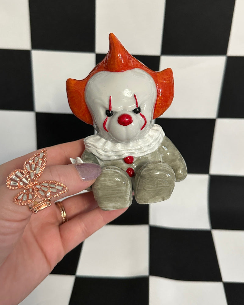 Hand holding a small clown figurine against a black and white checkered background