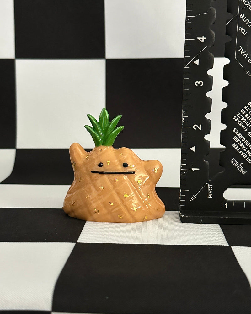 Pineapple-shaped figurine on a black and white checkered background with a ruler for scale.