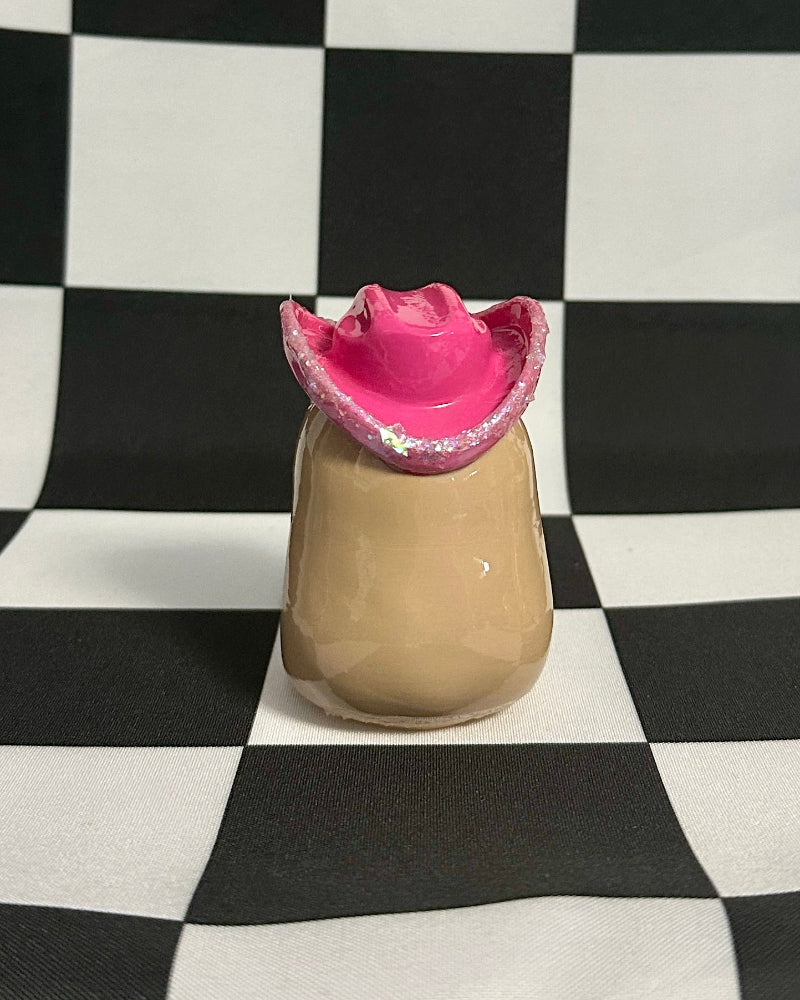 Small beige capybara with a pink hat on a black and white checkered background