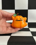 Hand holding a small orange pumpkin-shaped toy with a face on a black and white checkered background