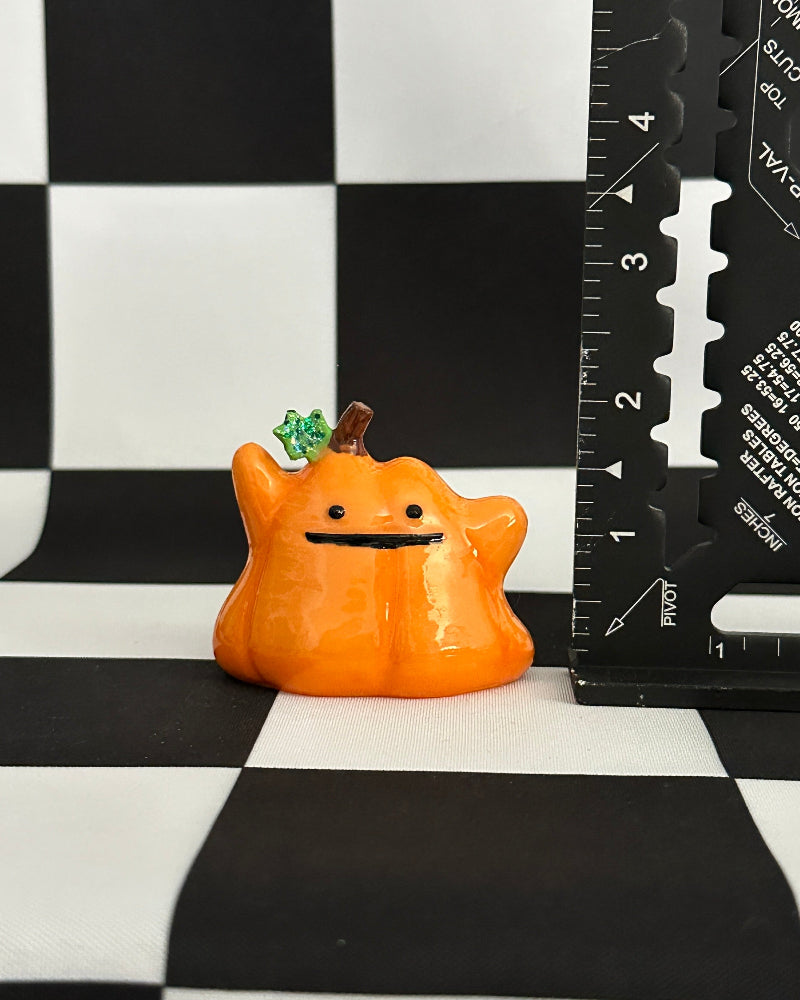 Small orange creature figurine on a black and white checkered surface with a ruler for scale.