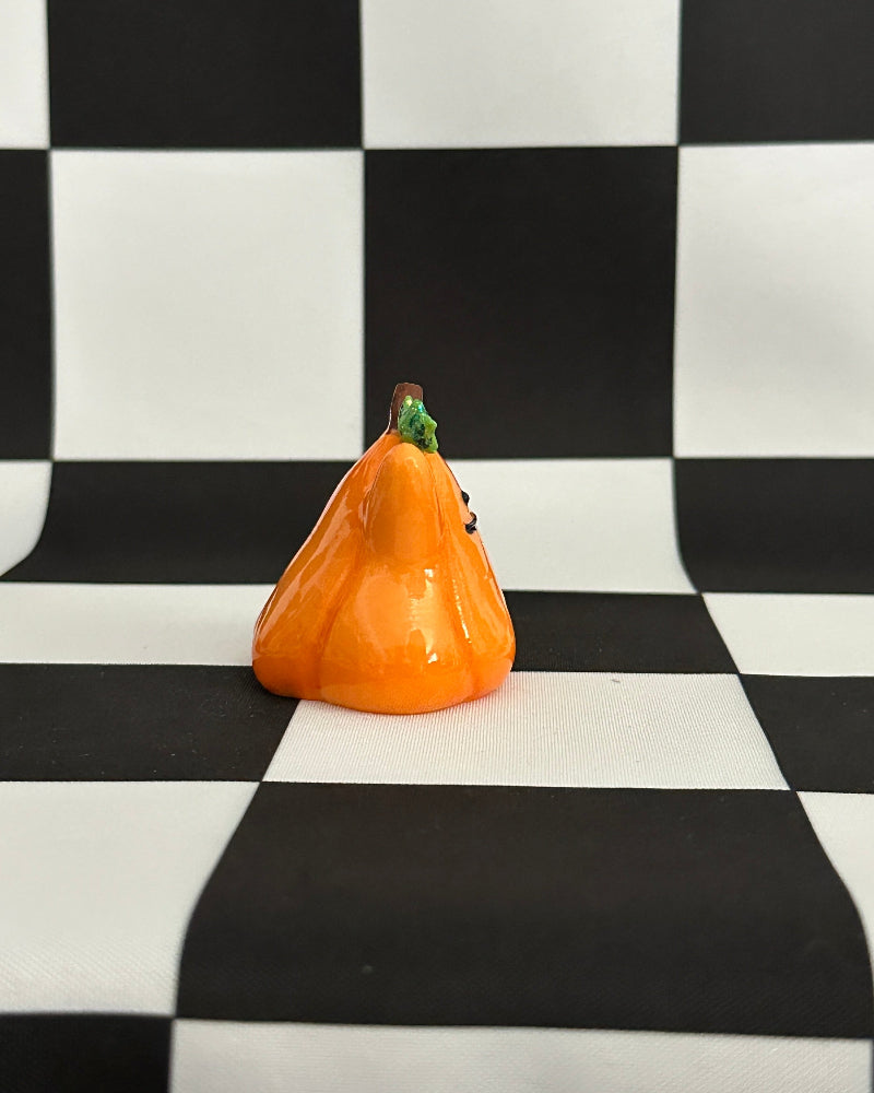Small orange pumpkin figurine on a black and white checkered background