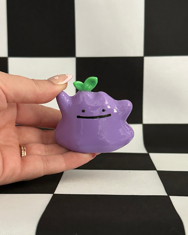 Purple character figurine held in a hand against a black and white checkered background