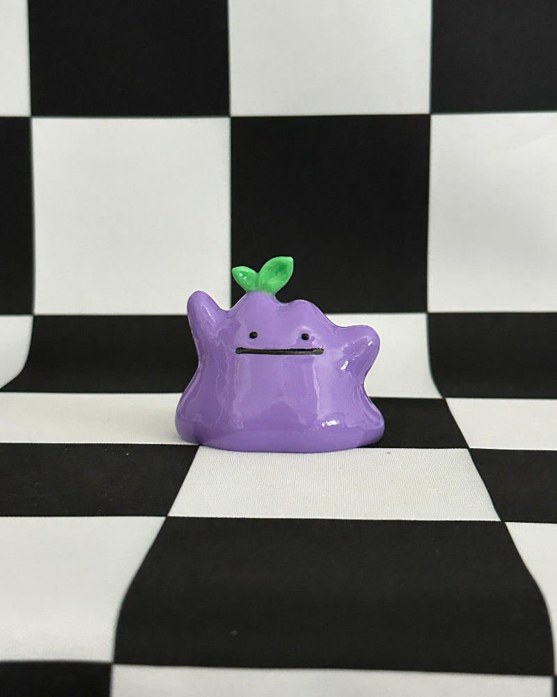 Purple cartoon-like creature with a green leaf on a black and white checkered background