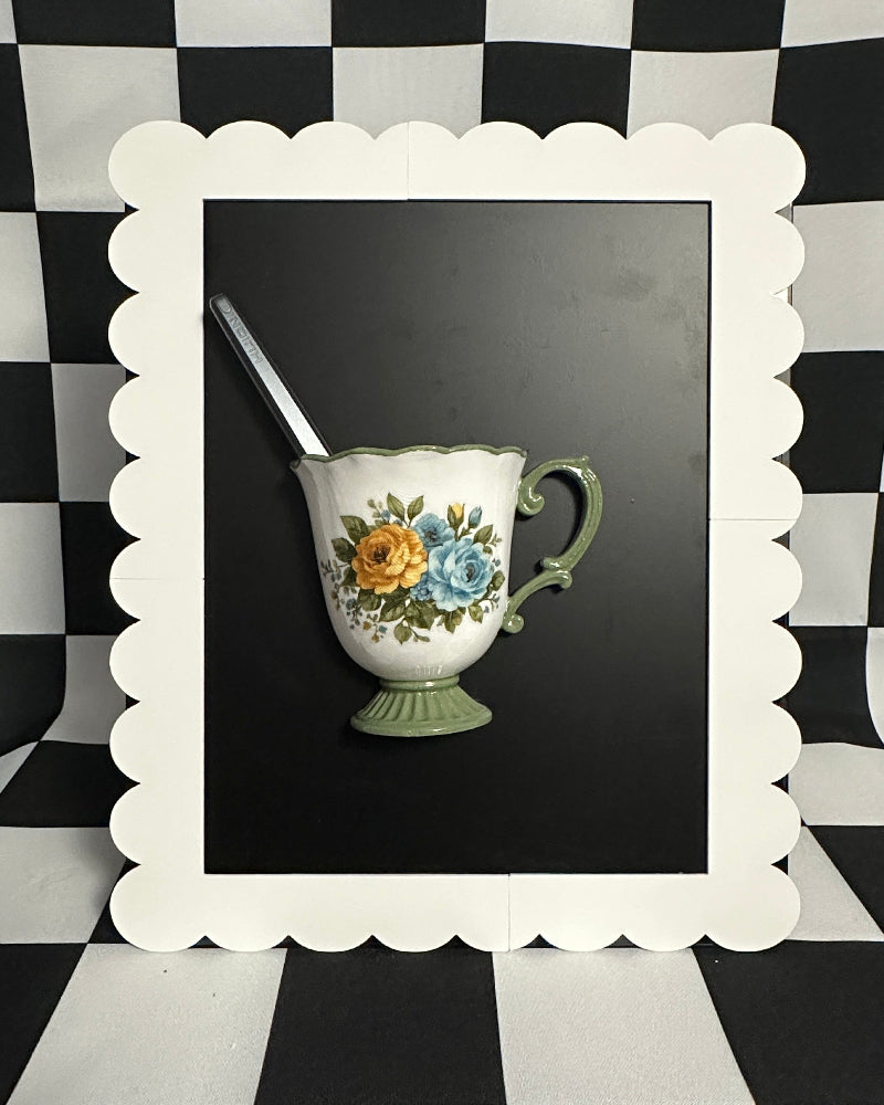 Decorative floral teacup with spoon in a white frame on a black and white checkered background