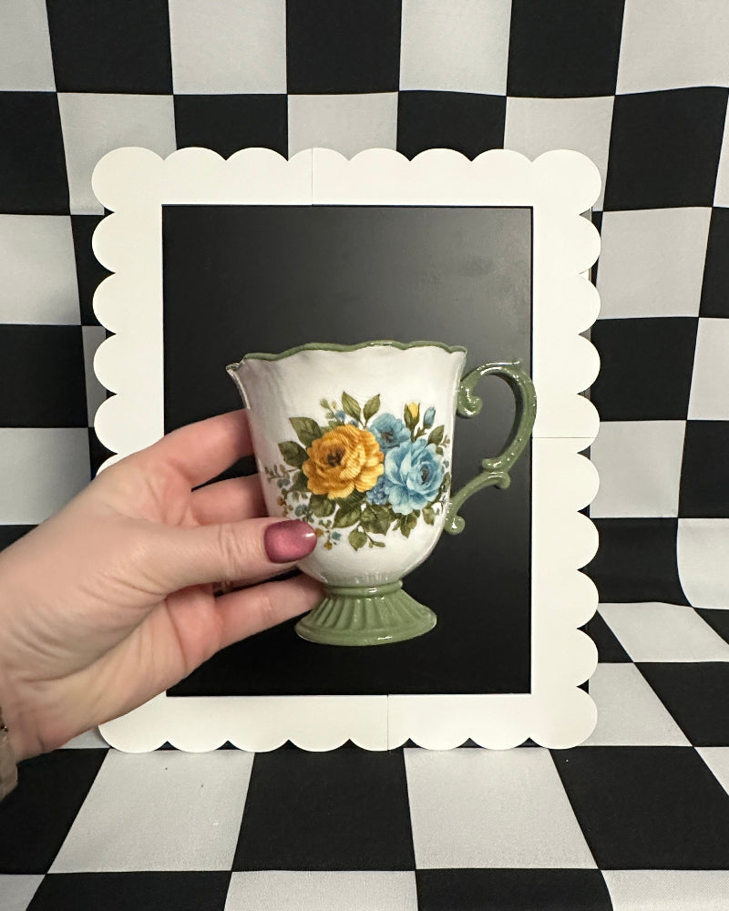 Hand holding a decorative teacup with floral design against a black and white checkered background.