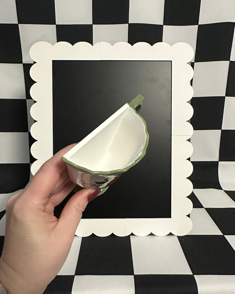 Hand holding a small ceramic dish against a black and white checkered background