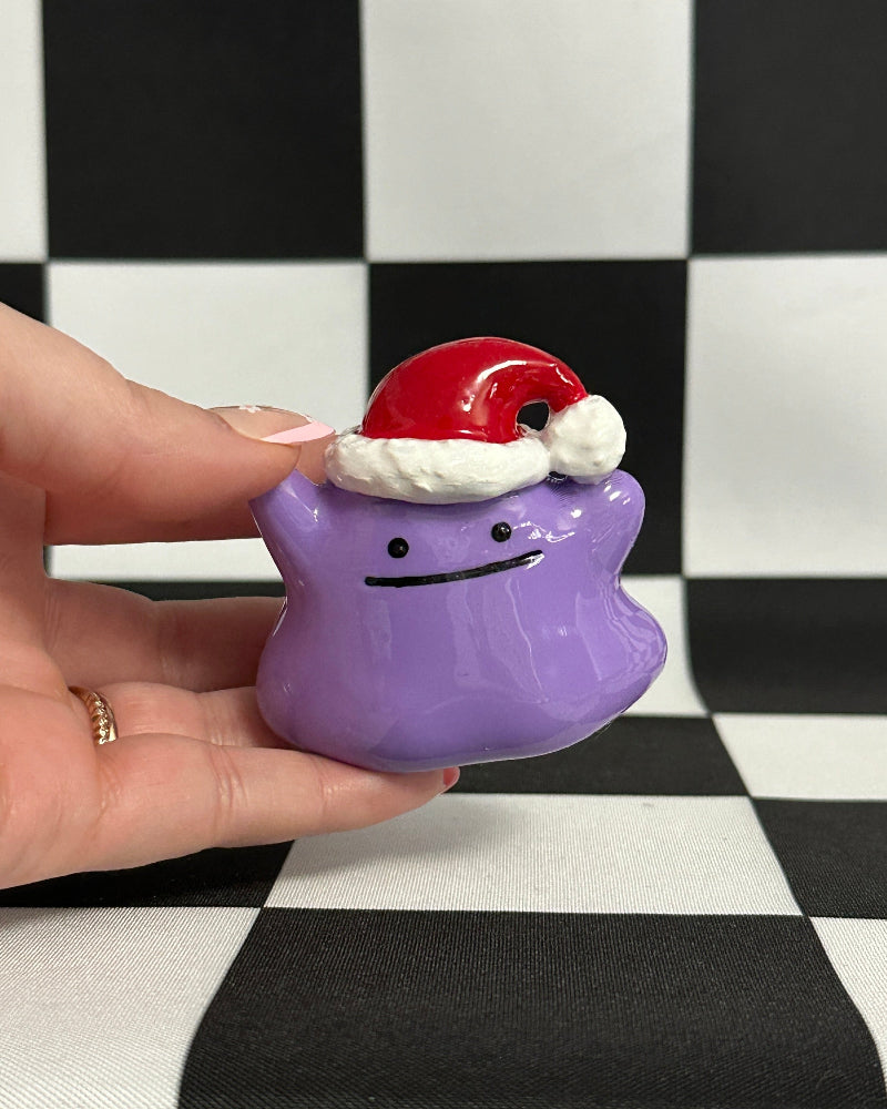 Purple ghost figurine with Santa hat held by a hand on a checkered background