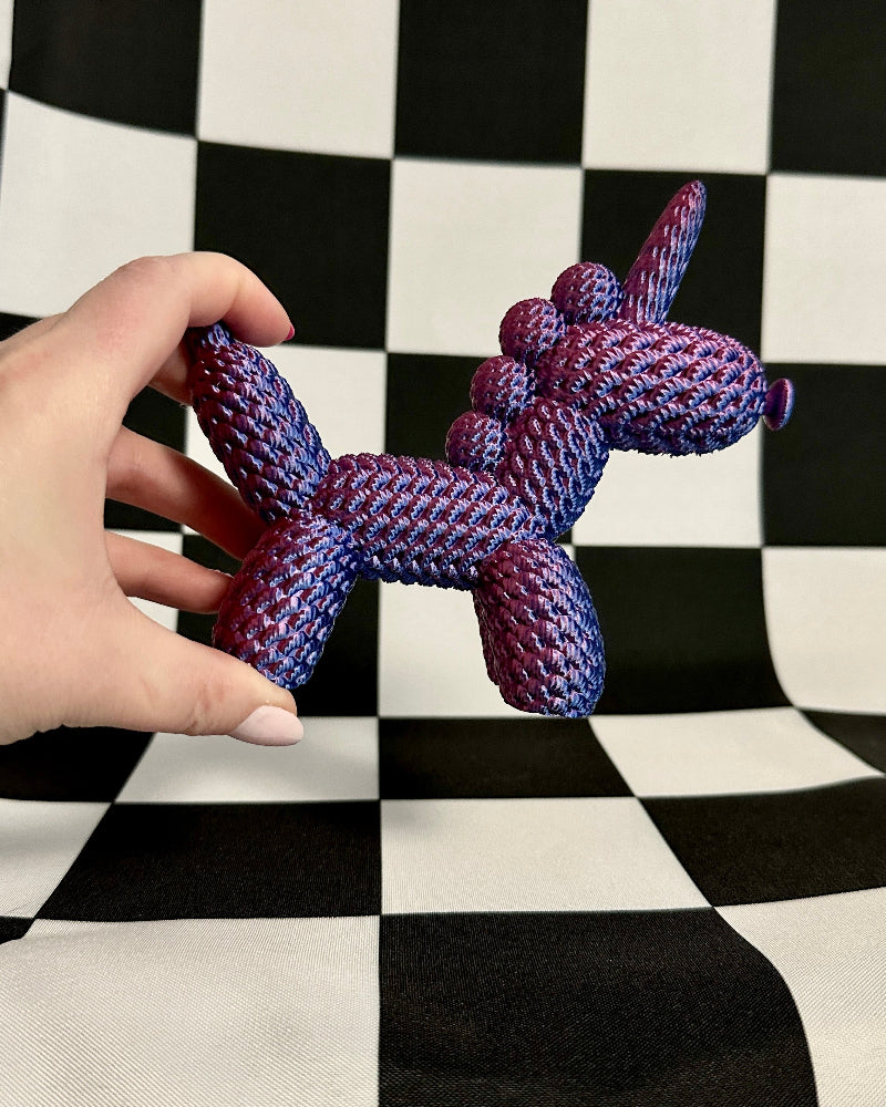 Hand holding a knitted purple dog toy against a black and white checkered background