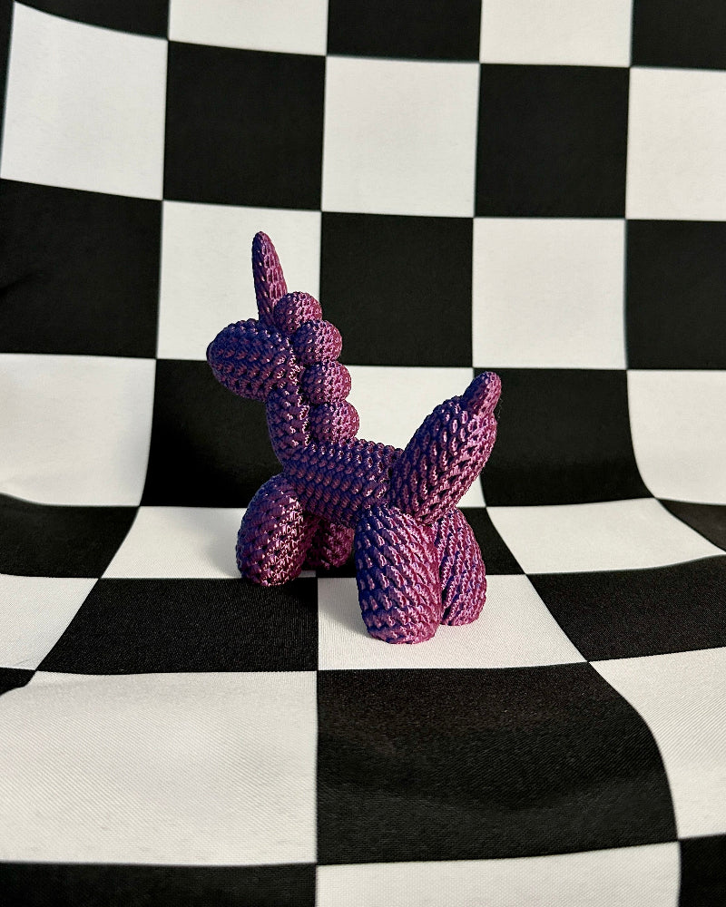 Purple knitted unicorn toy on a black and white checkered background