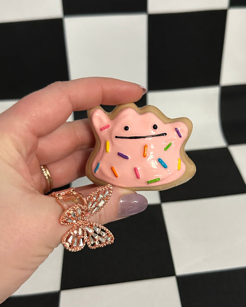 Hand holding a small ditto cookie with colorful design on a black and white checkered background