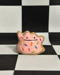 Pink creature figurine with rainbow sprinkles on a black and white checkered background