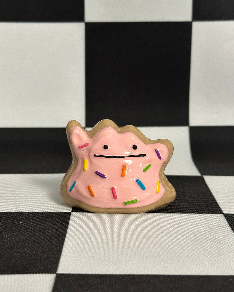 Pink creature figurine with rainbow sprinkles on a black and white checkered background