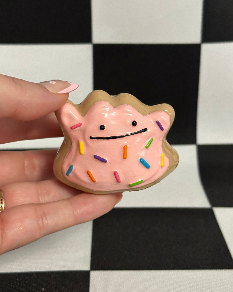 Hand holding a small pig-shaped cookie with sprinkles on a checkered background