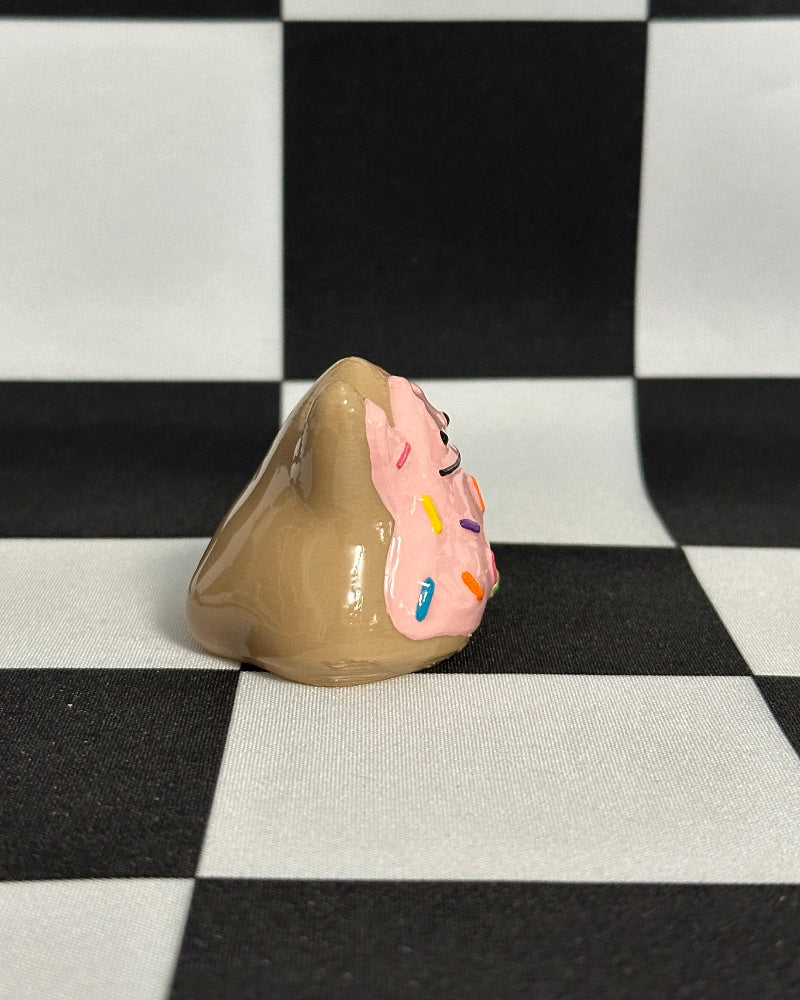 Decorative ceramic piece shaped like a cookie with pink icing and sprinkles on a black and white checkered background.