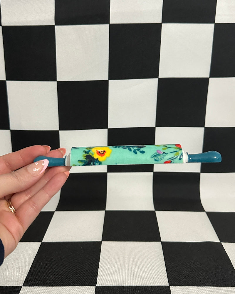 Hand holding a floral-patterned pen against a checkered background