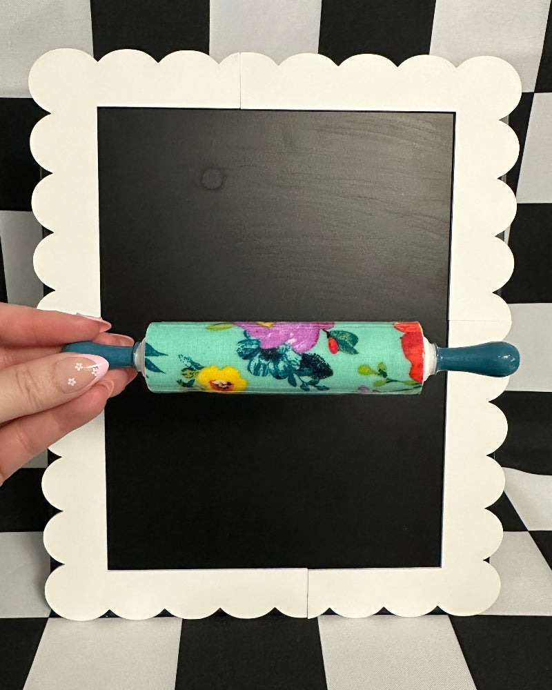 Hand holding a floral-patterned rolling pin against a blackboard with a checkered background