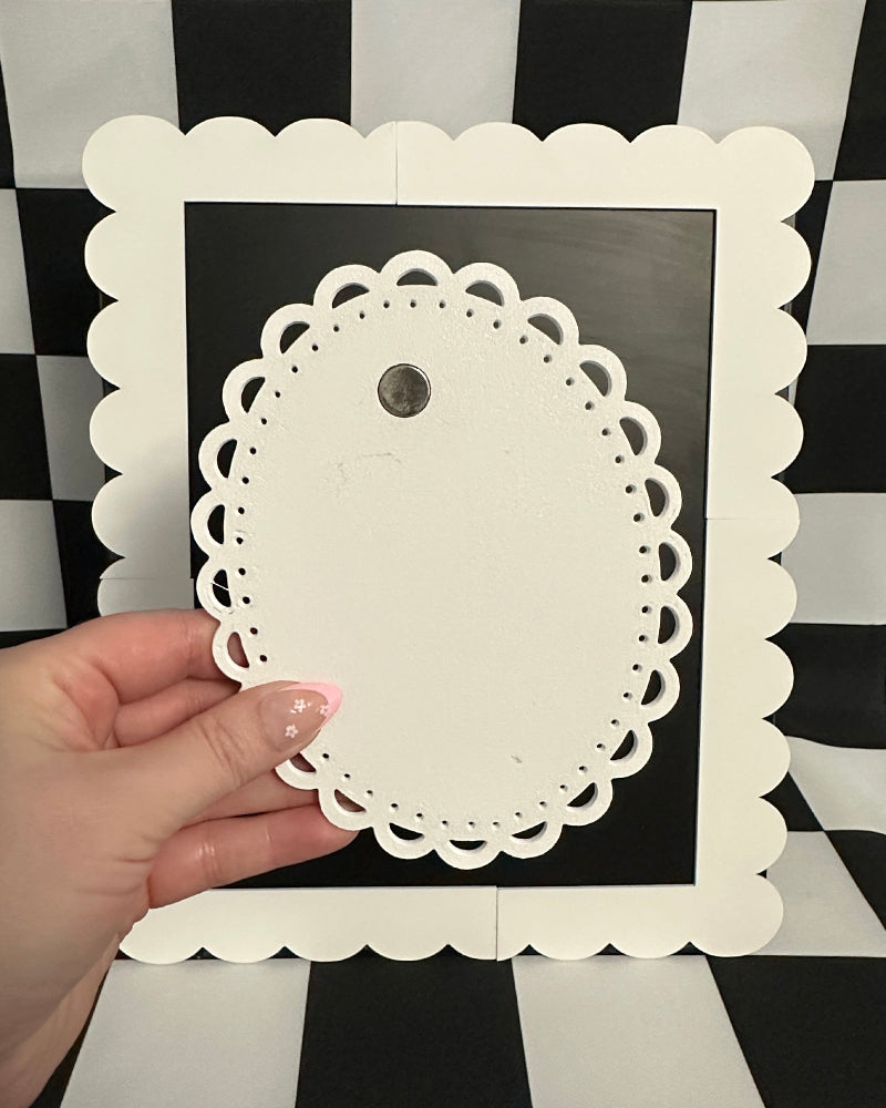 Hand holding a decorative white doily against a black and white checkered background