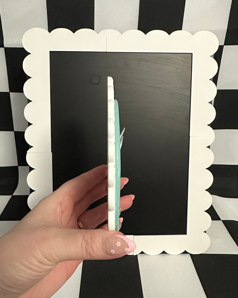 Hand holding a pen over a blackboard with a decorative white frame on a black and white checkered background.