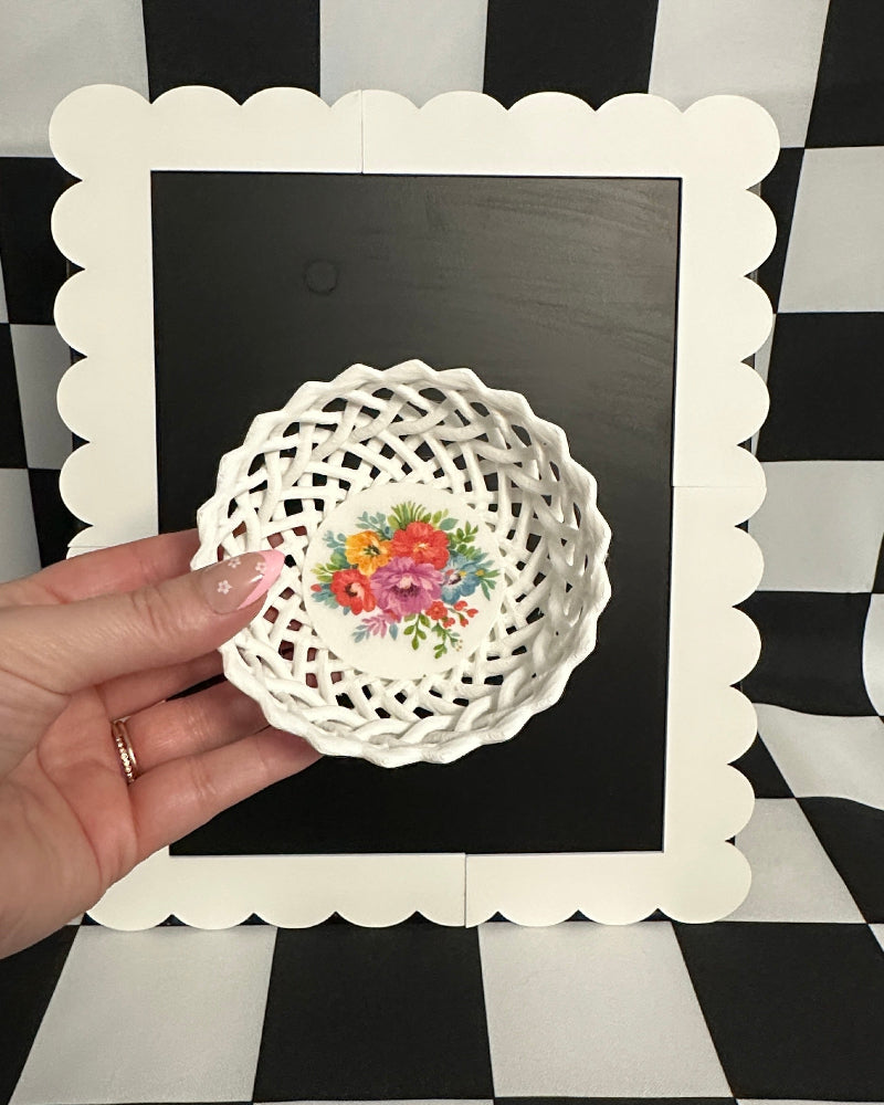 Hand holding a decorative lace doily with floral design on a black and white checkered background