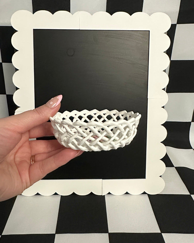 White decorative basket held by a hand in front of a blackboard on a black and white checkered background