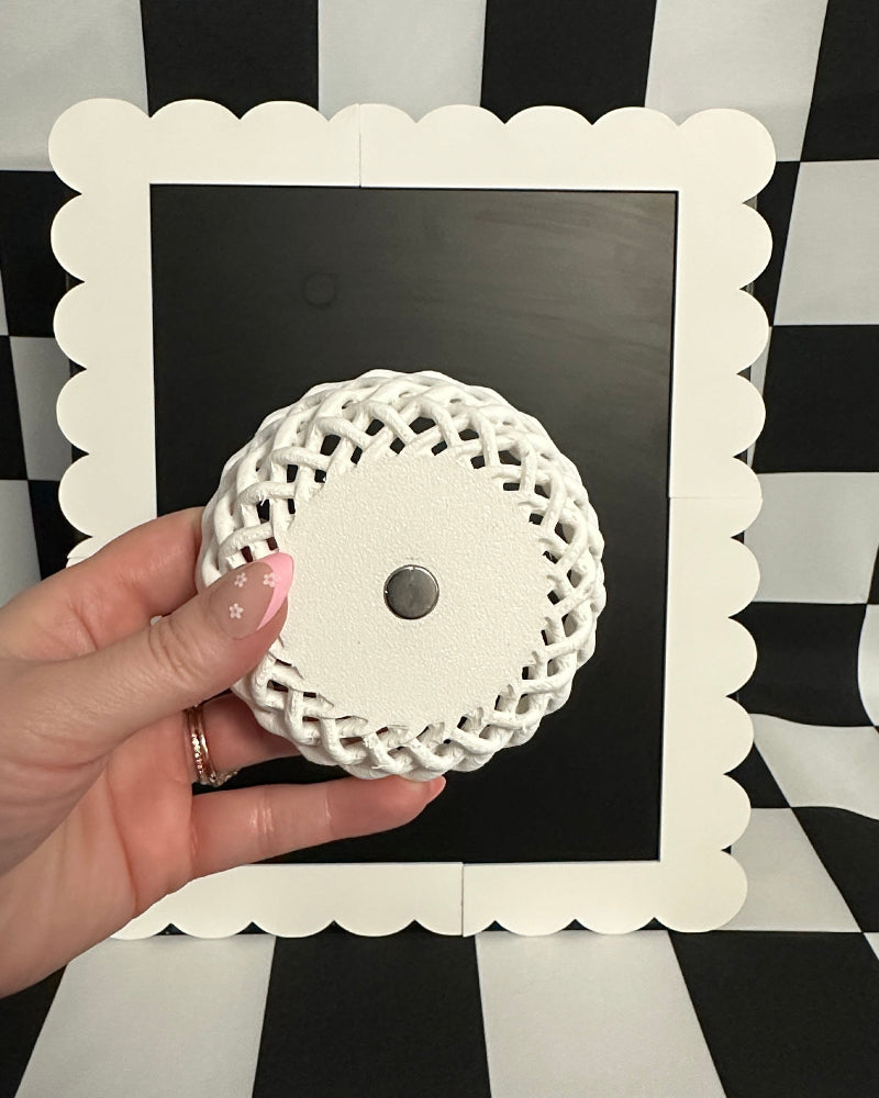 Hand holding a decorative white object against a black and white checkered background
