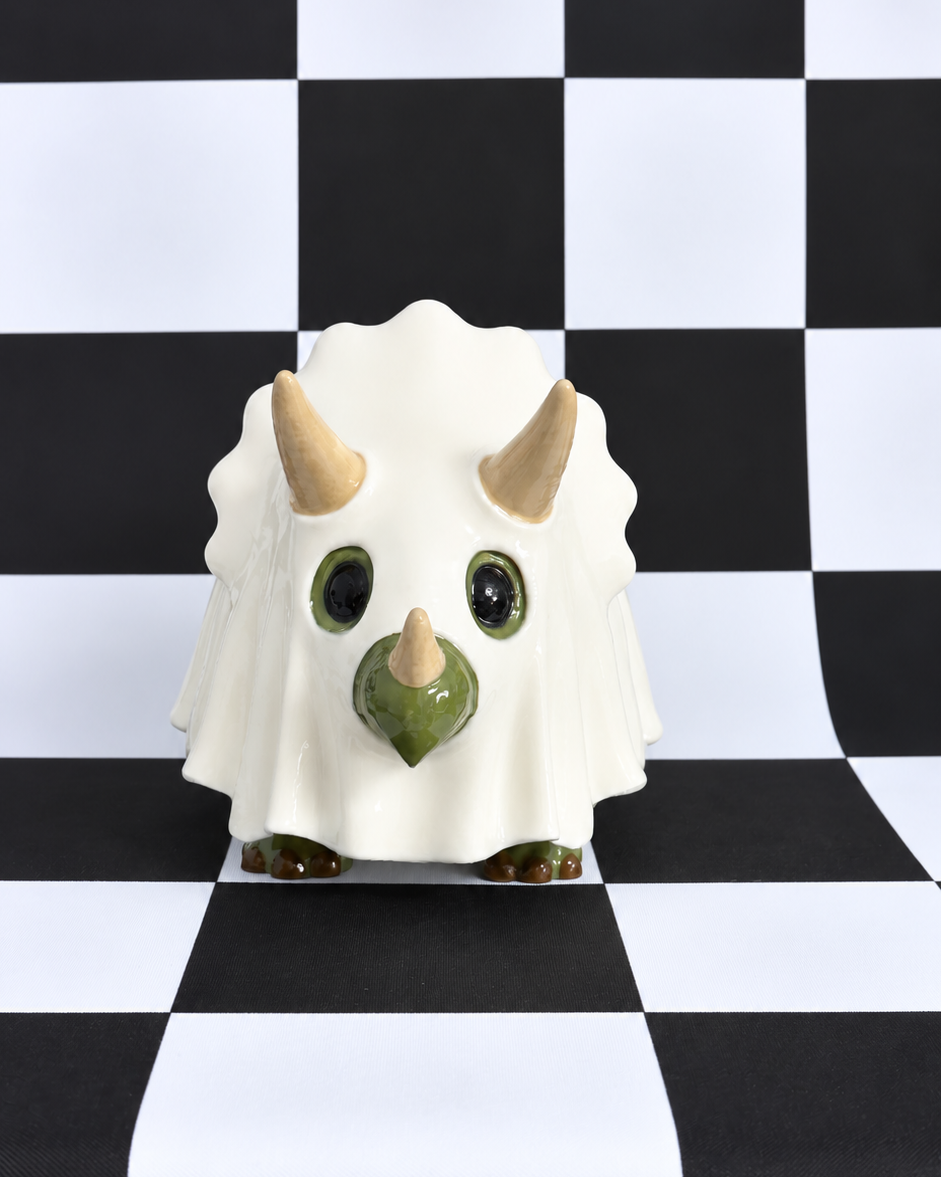 A small white ceramic dinosaur figurine with green accents and beige horns, standing on a black and white checkered surface.