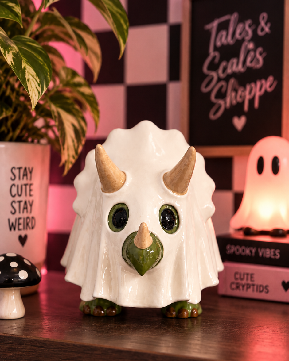 A white ceramic Triceratops toy figurine with green accents and gold horns, displayed on a wooden shelf in a cozy, dimly lit room with plants, a sign reading 'Tales & Scales Shoppe', and a glowing ghost lamp.