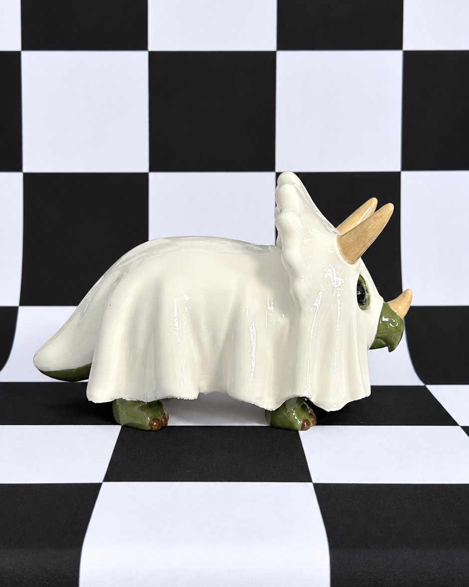 A ceramic Triceratops figurine dressed in a white ghost costume, standing on a black and white checkered background.