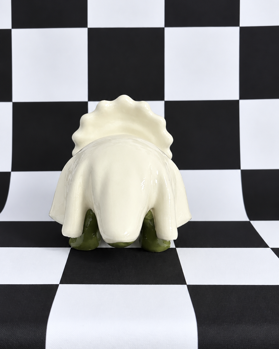 A small decorative figurine or sculpture with a cream-colored shell-like top and green legs, photographed against a black-and-white checkered backdrop.