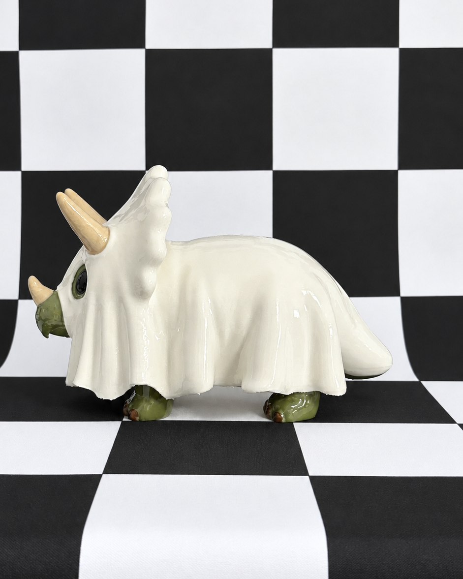 A ceramic Triceratops figurine with a glossy white body, green legs, and beige horns, standing on a black and white checkered surface.