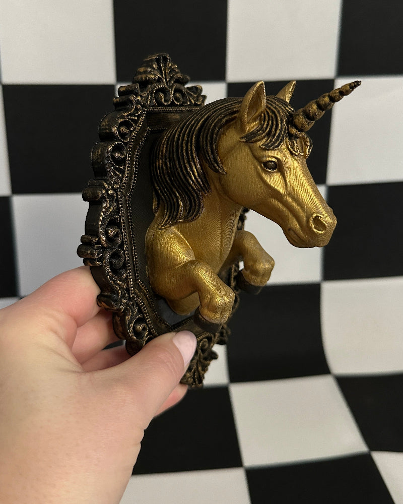 Gold unicorn figurine with decorative frame held against a black and white checkered background